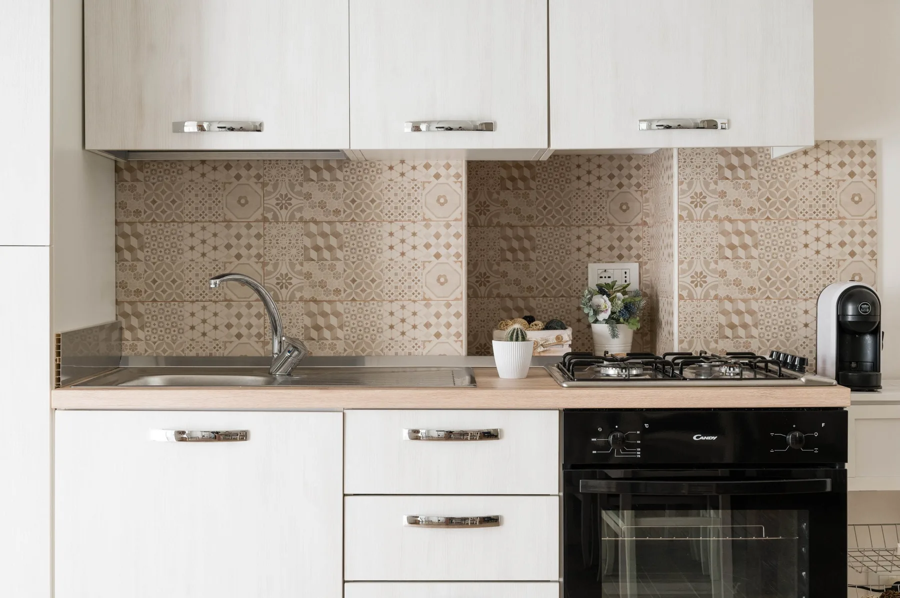 A kitchen counter with a sink, cooktop, and oven beneath white cabinets.