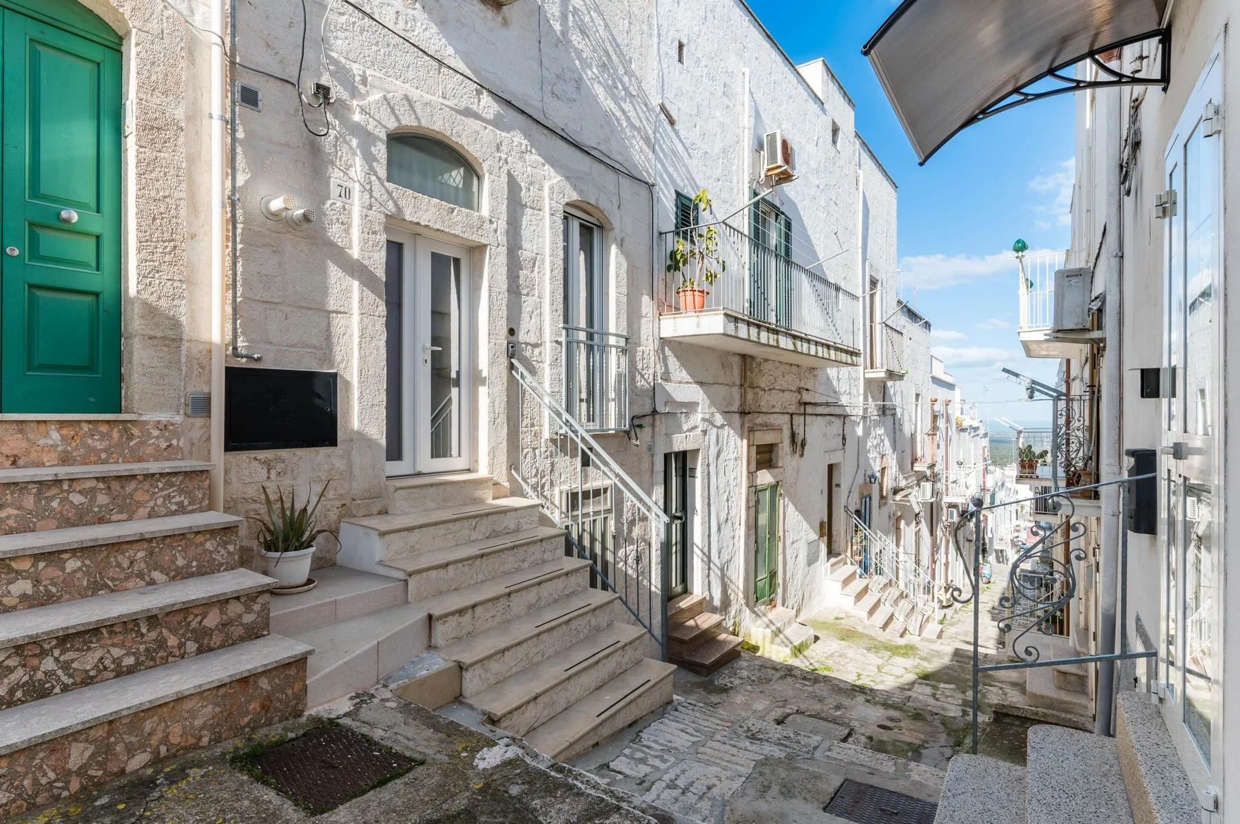 A narrow stone-paved street runs between white buildings, with steps leading to a green doorway.