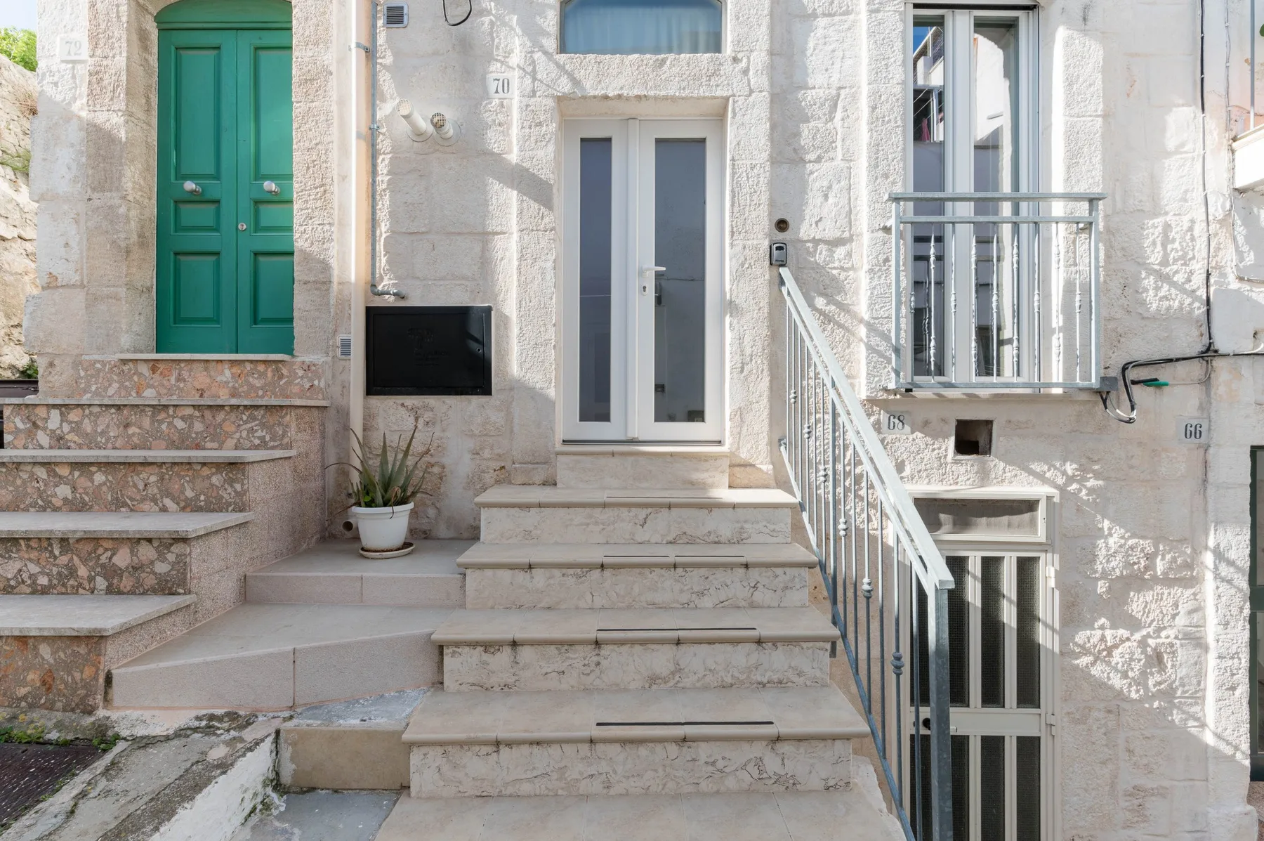 Stone building entrance with steps, a green door, and a white-framed glass door.