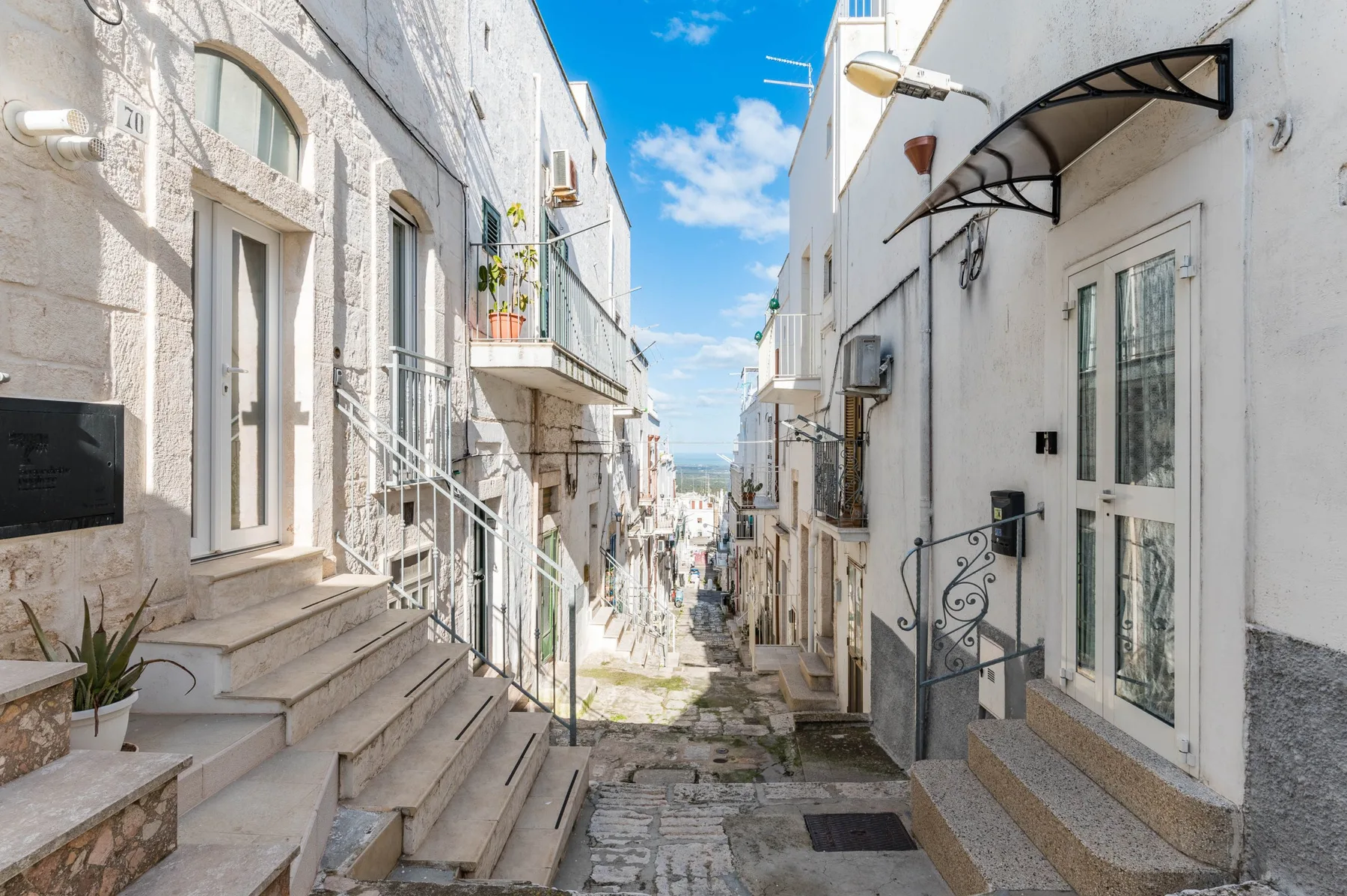 A narrow stone-paved street runs between closely spaced white buildings.