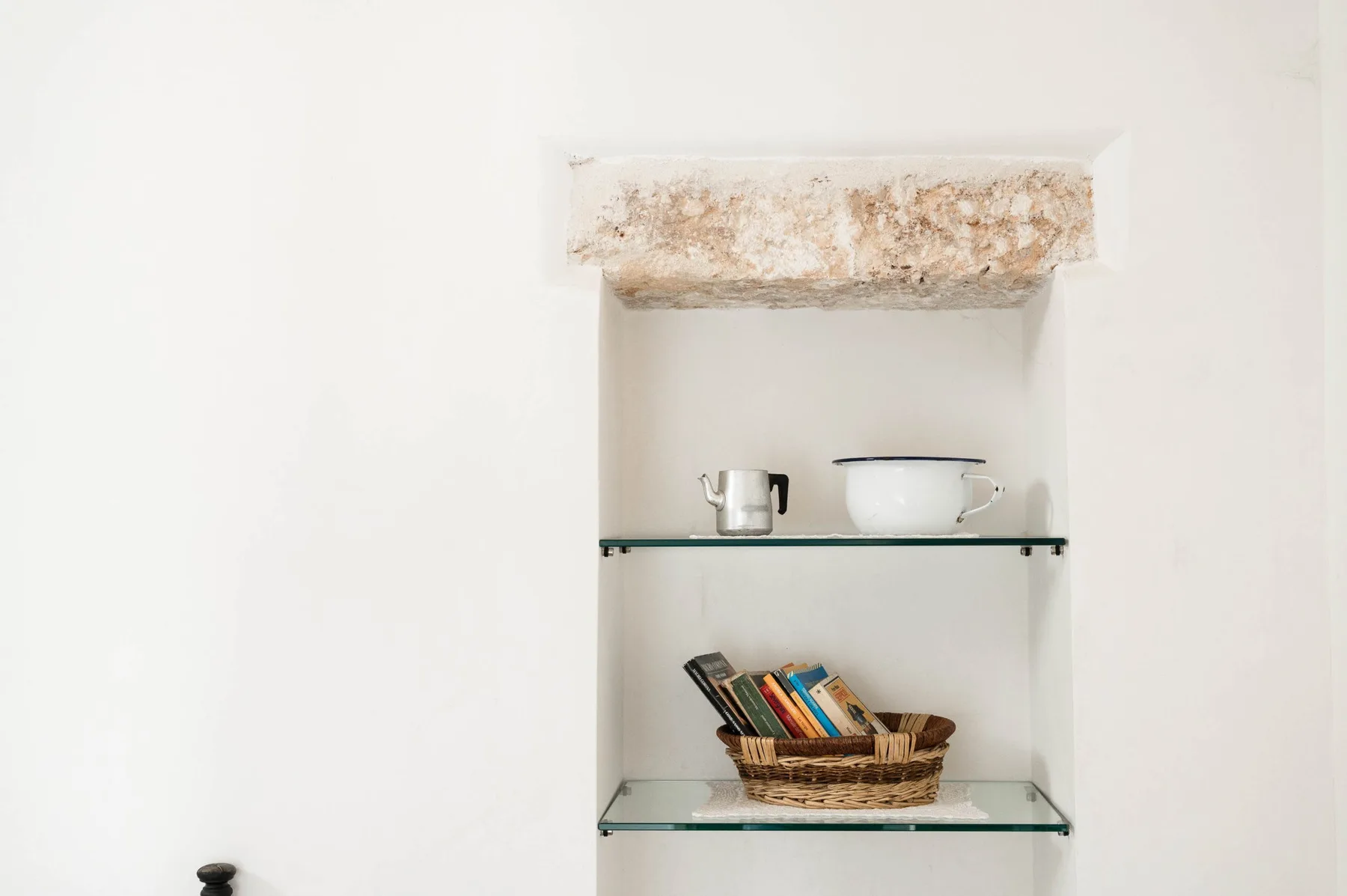 A recessed wall shelf displays a kettle, a pot, and a basket of books.