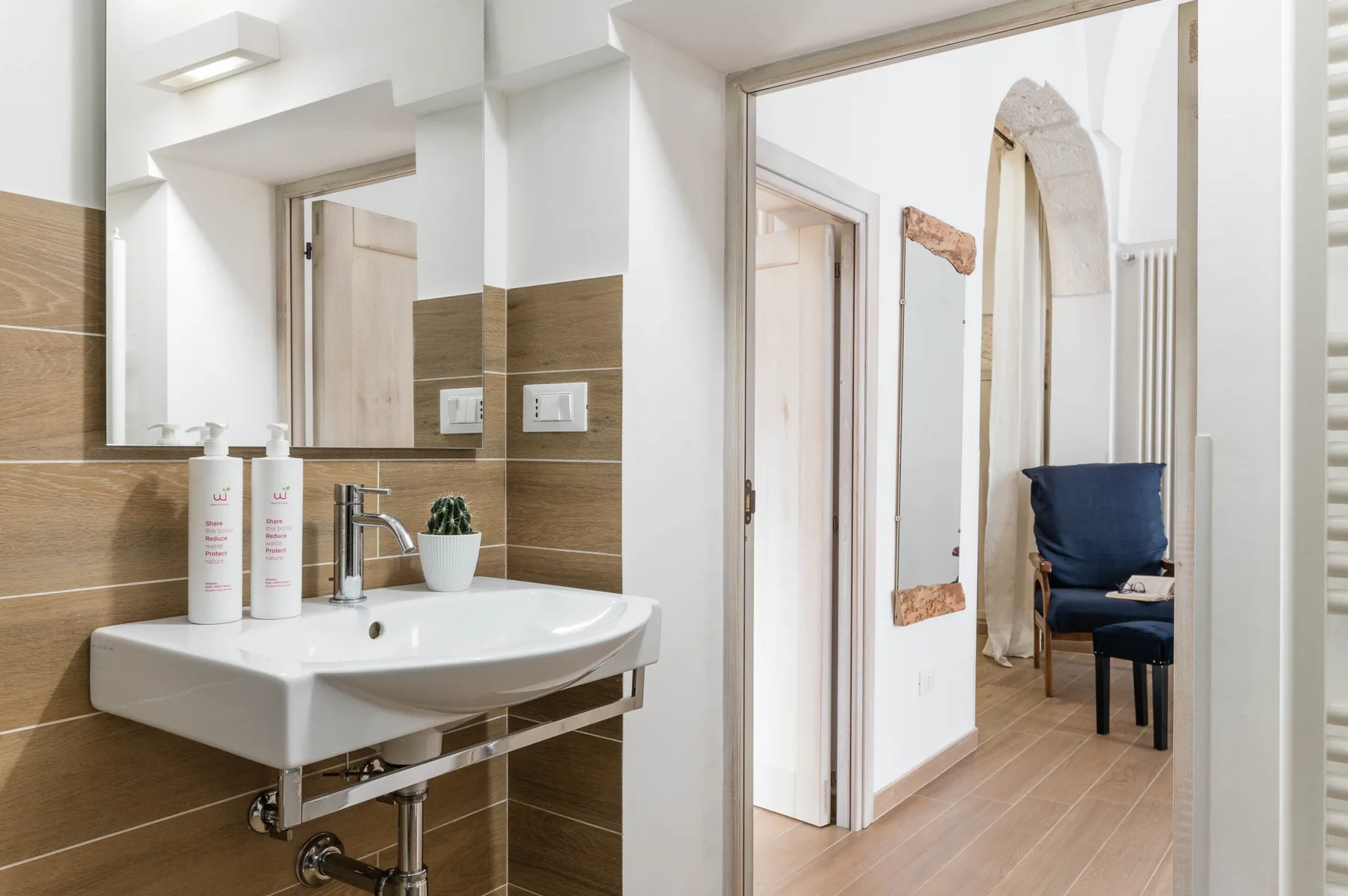 A bathroom sink opens onto a hallway with a blue chair.