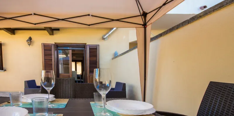 A dining table with glassware sits beneath a canopy in an outdoor courtyard.