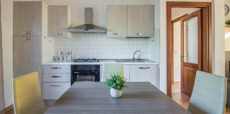 A modern kitchen with pale cabinets and a dining table in the foreground.
