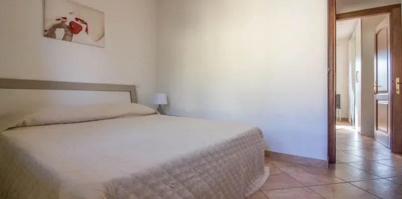 A bedroom with a neatly made bed and an open doorway.
