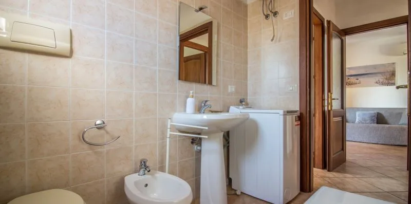 A tiled bathroom with a sink and a doorway opening onto a bedroom.