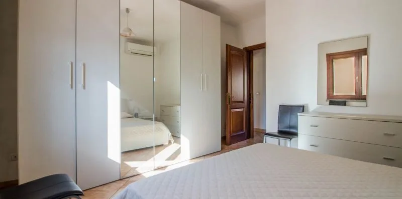 A bright bedroom with a bed, mirrored wardrobe, and dresser.