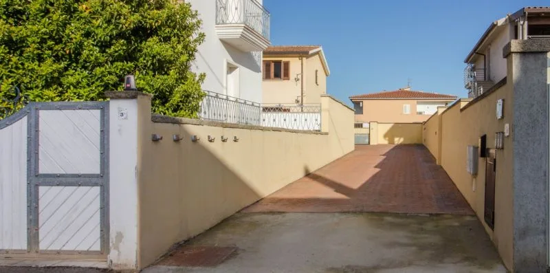 A paved driveway runs between residential buildings toward a closed gate.