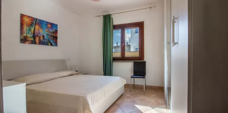 A bedroom with a bed, a window, and a chair.