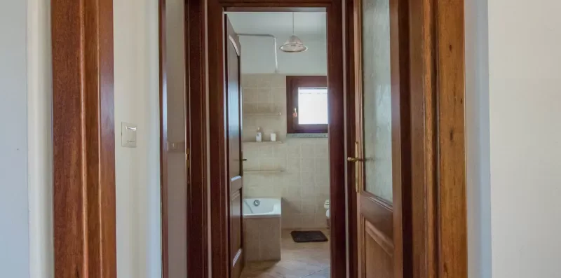 A hallway opens through wooden doorways toward a bathroom with a sink.