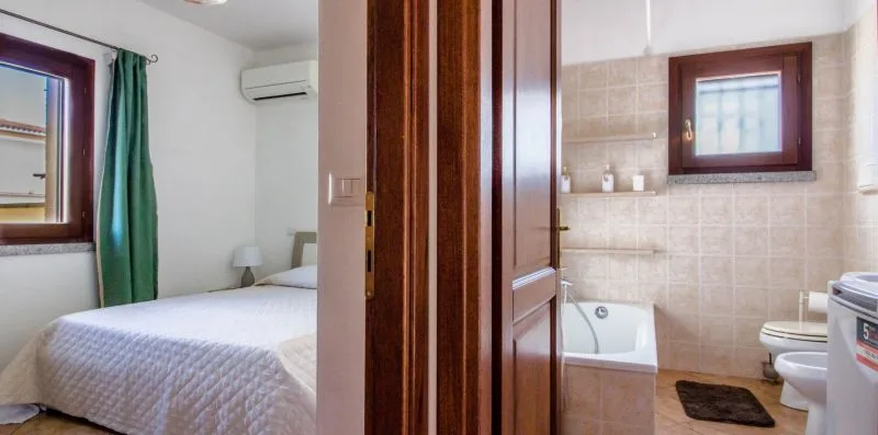 A bedroom and adjoining tiled bathroom are visible through an open doorway.