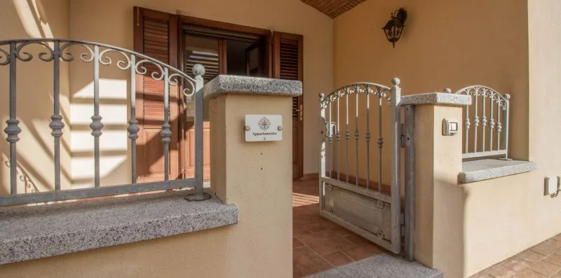 A tiled entrance porch with an open metal gate and a window with wooden shutters.