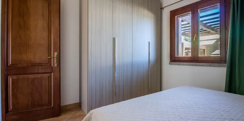 Bedroom with a bed, wardrobe, wooden door, and window.