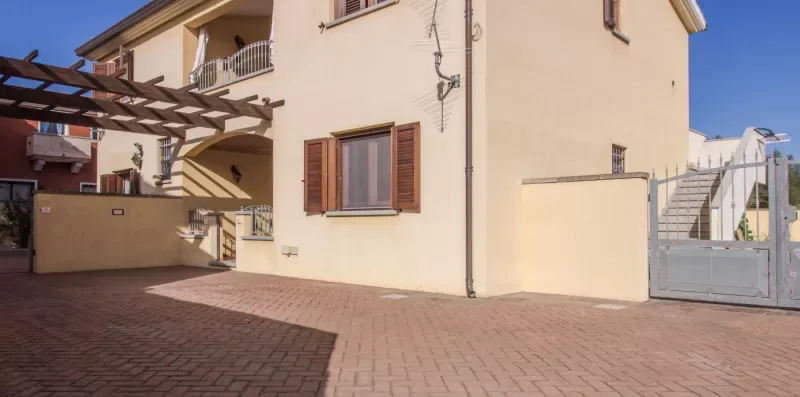 A paved courtyard beside a pale stucco building, with a wooden pergola overhead.
