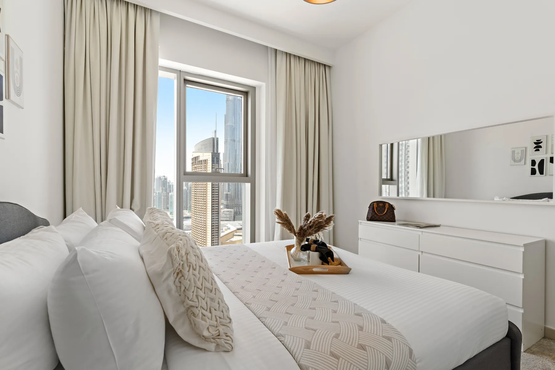 A bright bedroom with a neatly made bed beside a large curtained window.