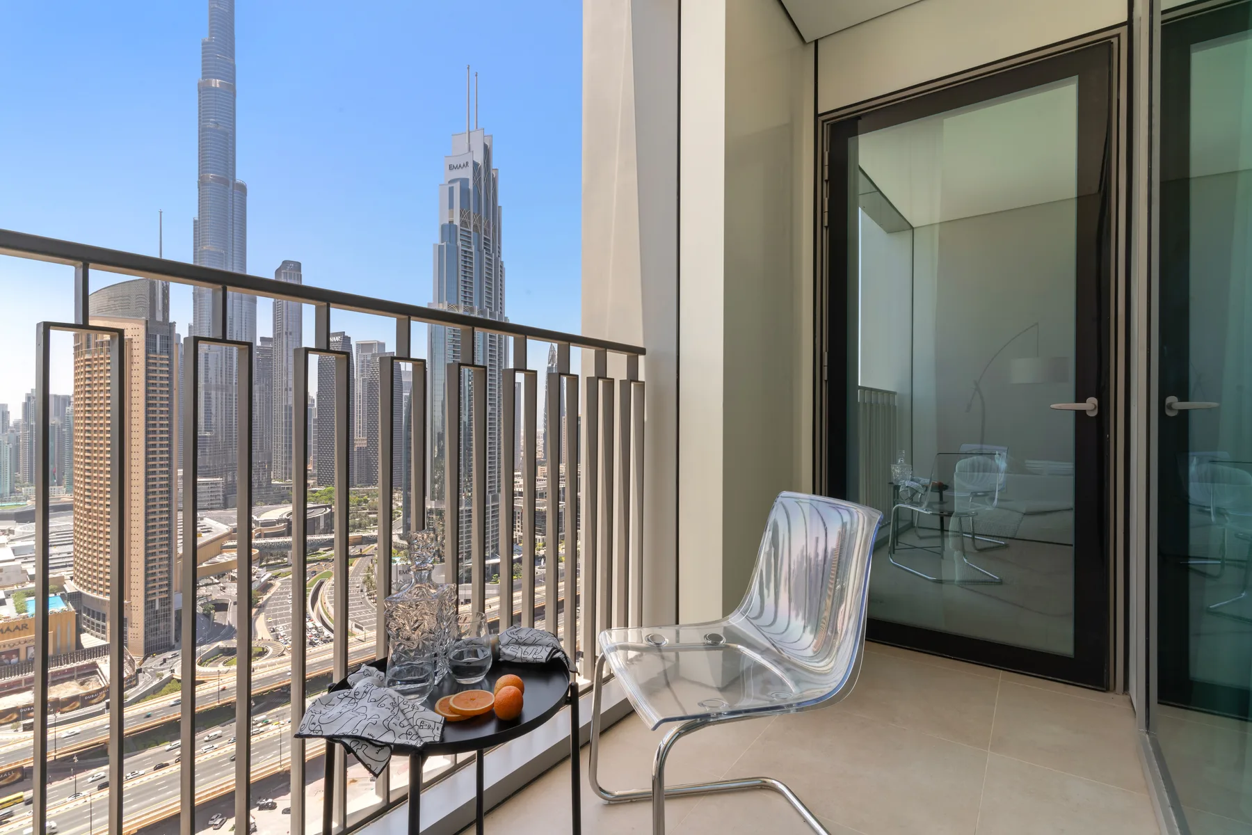A balcony with a small table and seating overlooks a city skyline.