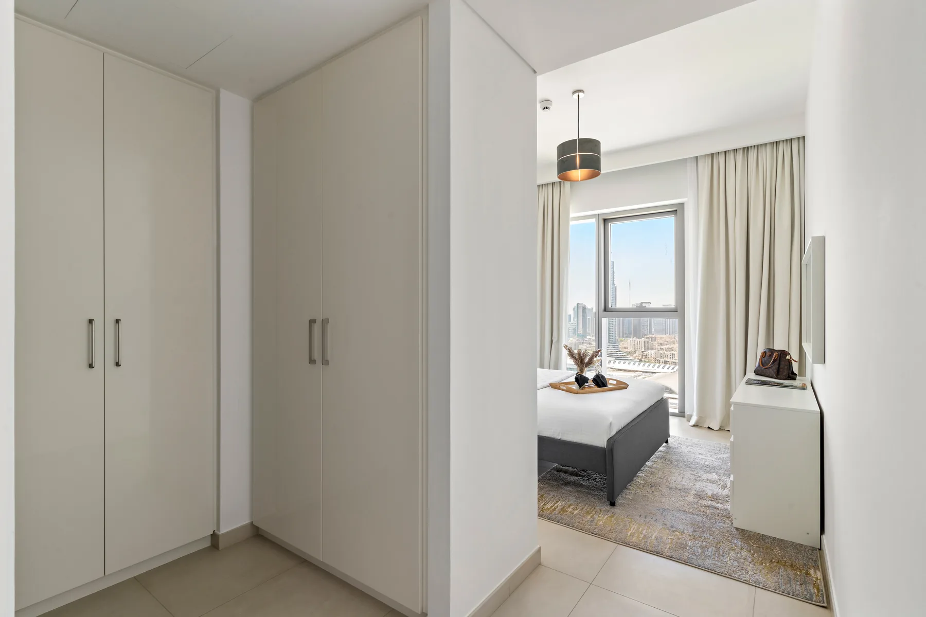 A bedroom with a bed, pale curtains, and a large window.