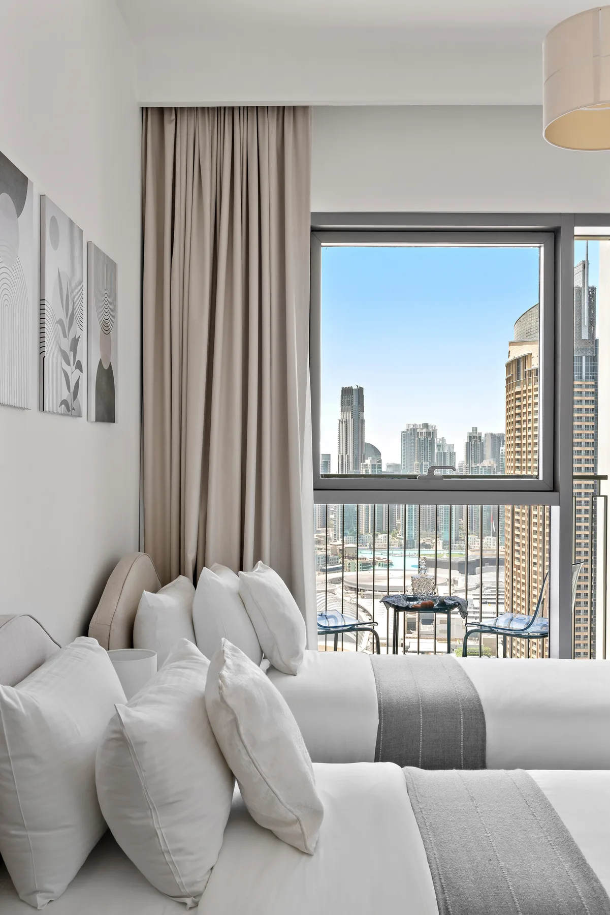 A bright bedroom with neatly made beds and a large window overlooking the city.