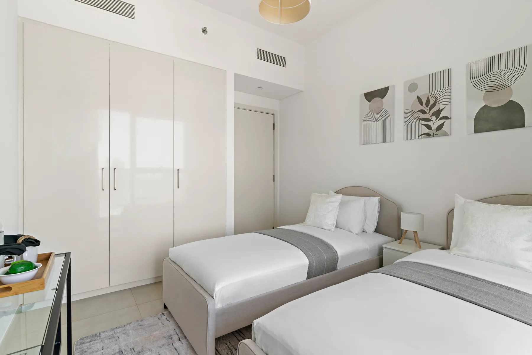A bright bedroom with two beds, a built-in wardrobe, and framed artwork.