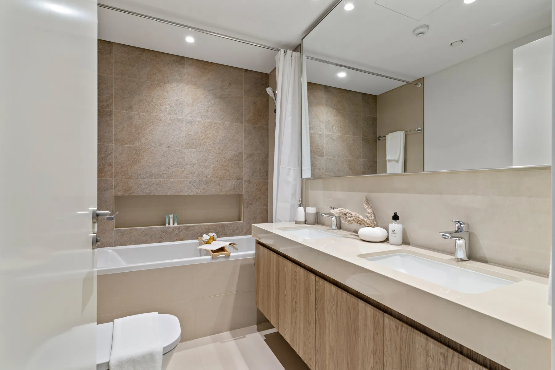 A modern bathroom with a bathtub, shower curtain, and long vanity.