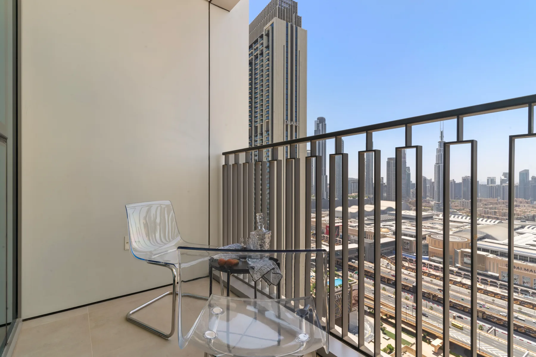 A balcony with clear seating overlooks city buildings and railway tracks.