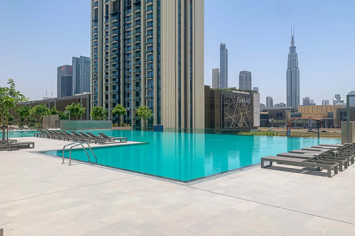 A rooftop swimming pool sits beside high-rise buildings under a clear sky.