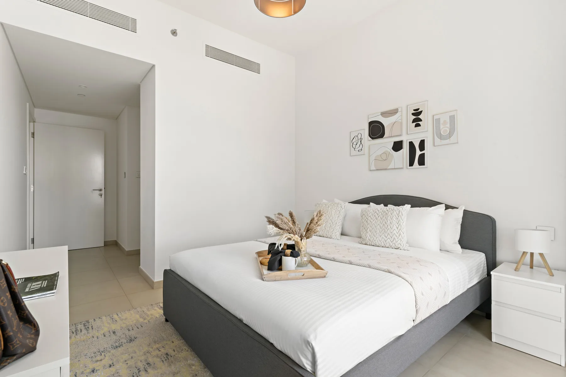 A bright bedroom with a neatly made bed and framed artwork above it.