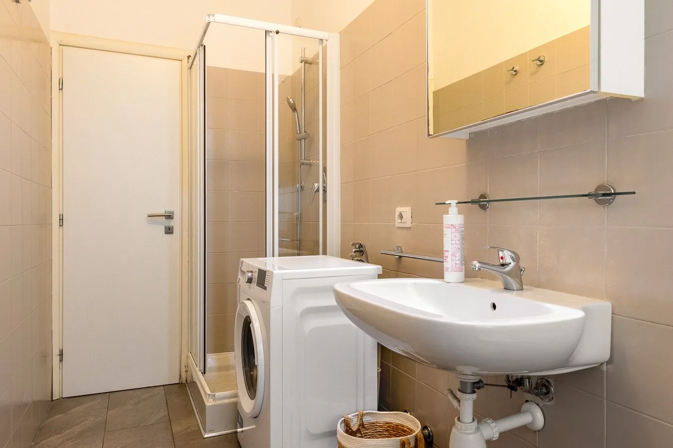 Un baño con azulejos, lavabo, ducha y lavadora.