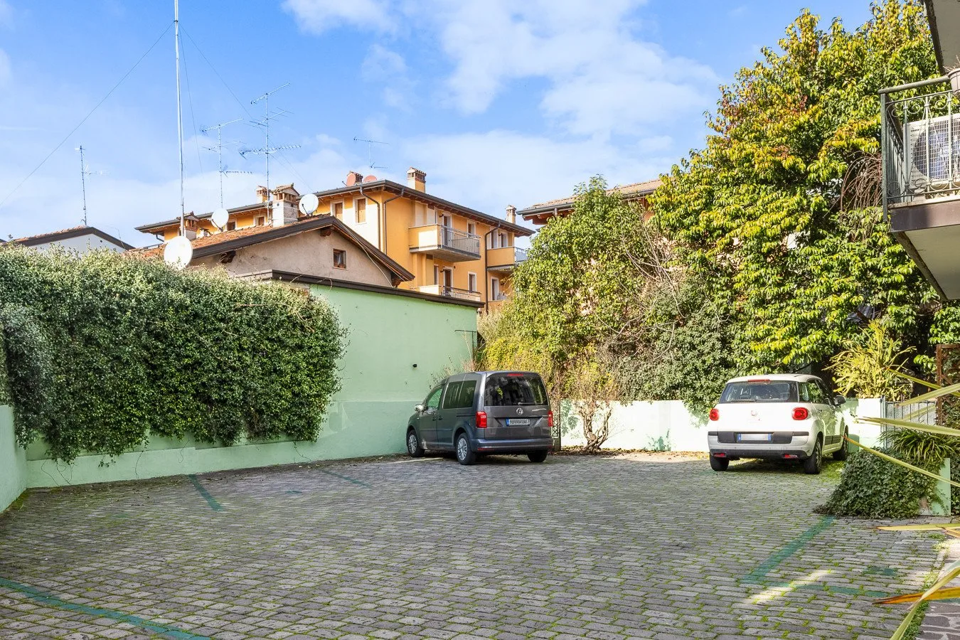 Una zona de estacionamiento pavimentada con dos vehículos junto a un muro verde.
