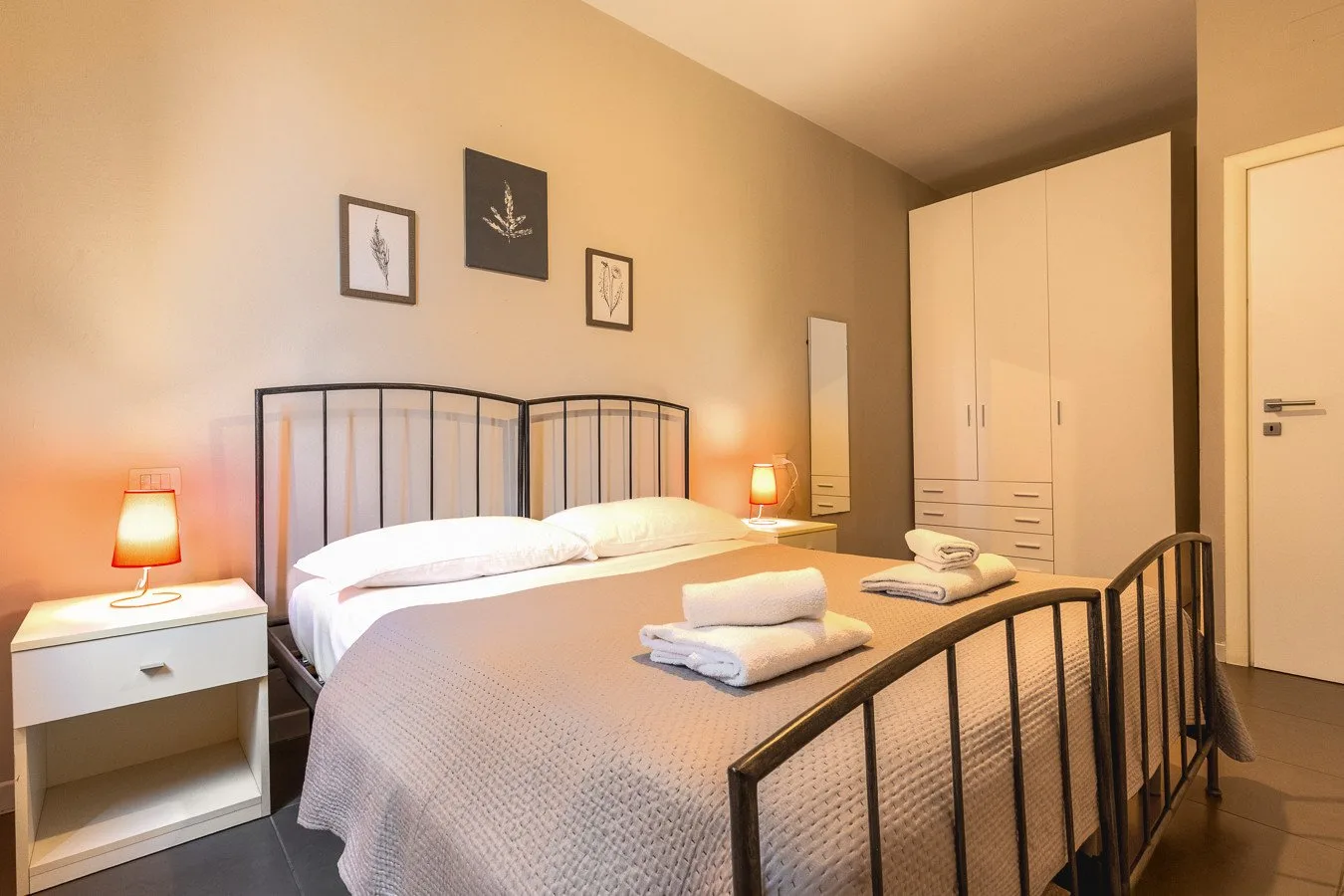 Un dormitorio con una cama de estructura metálica, ropa de cama blanca y lámparas de noche.
