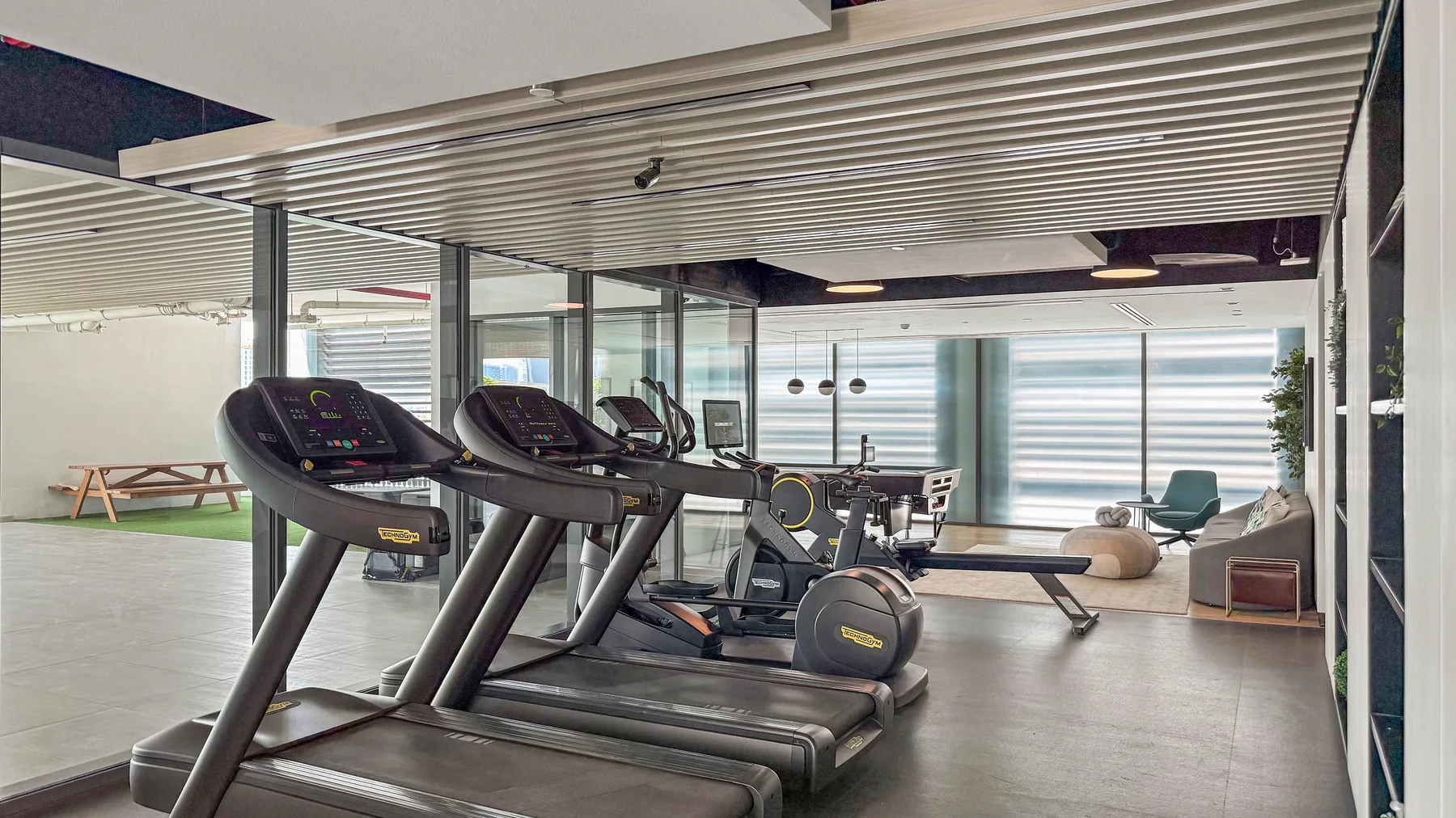 A gym with treadmills and exercise equipment beside large windows.