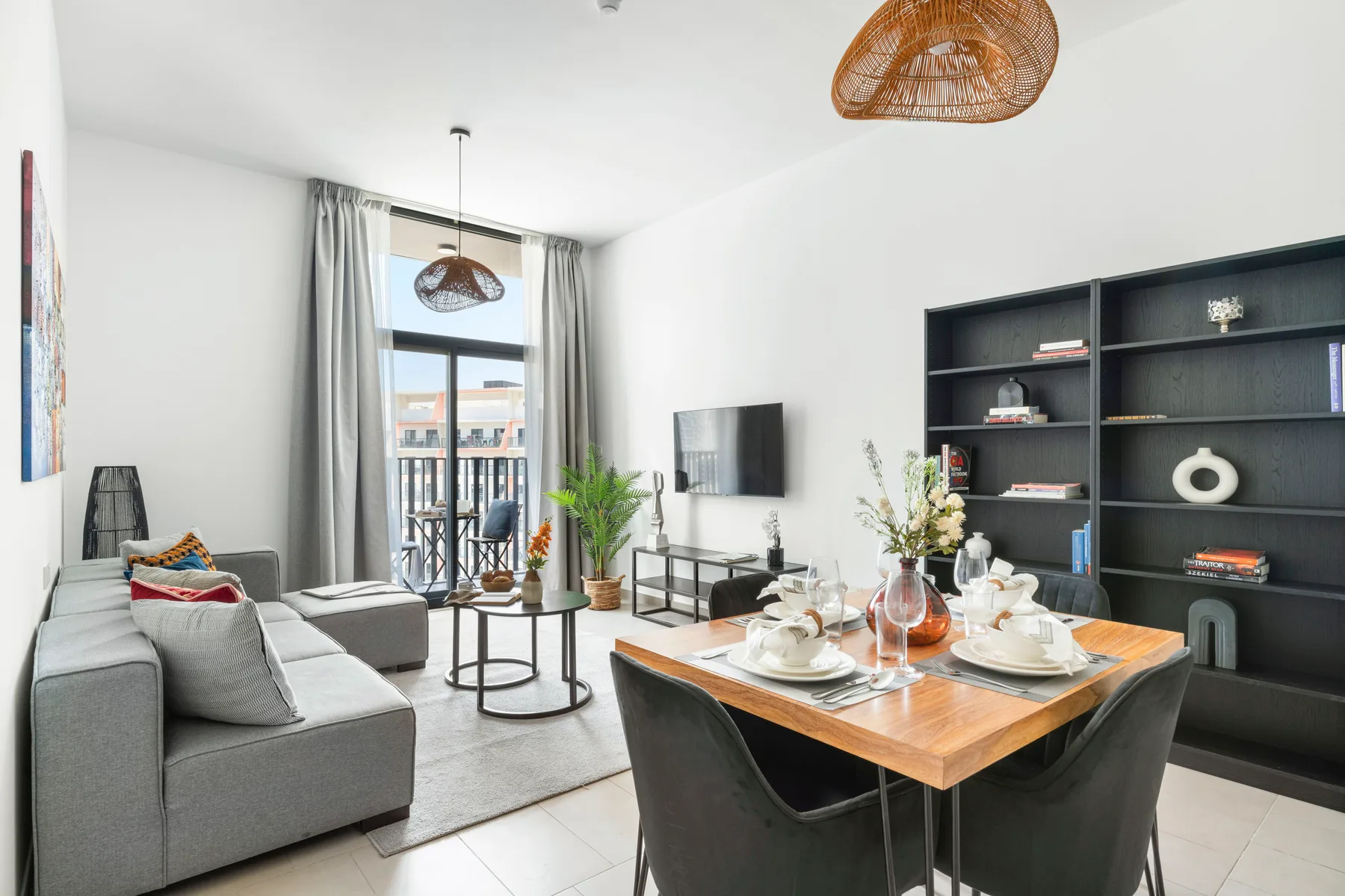 A bright living and dining room with a table set beside a large window.