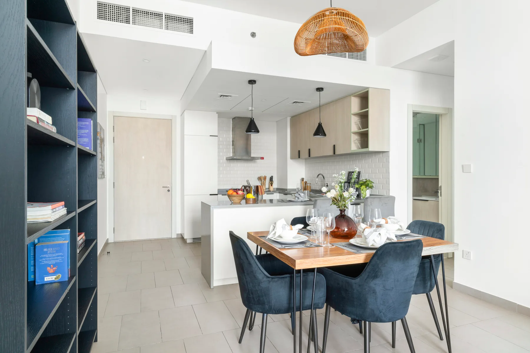A dining table sits beside an open kitchen with dark seating.