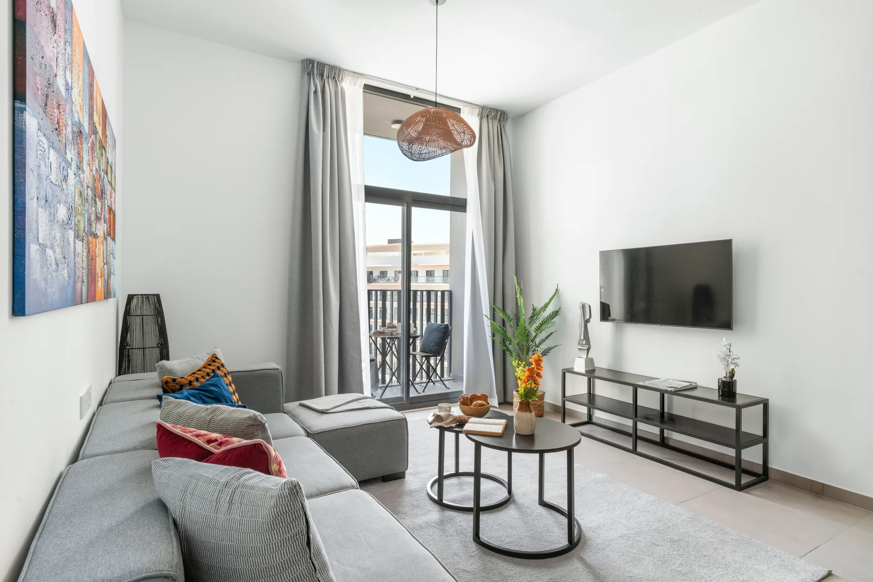 A bright living room with gray seating, a television, and a balcony window.