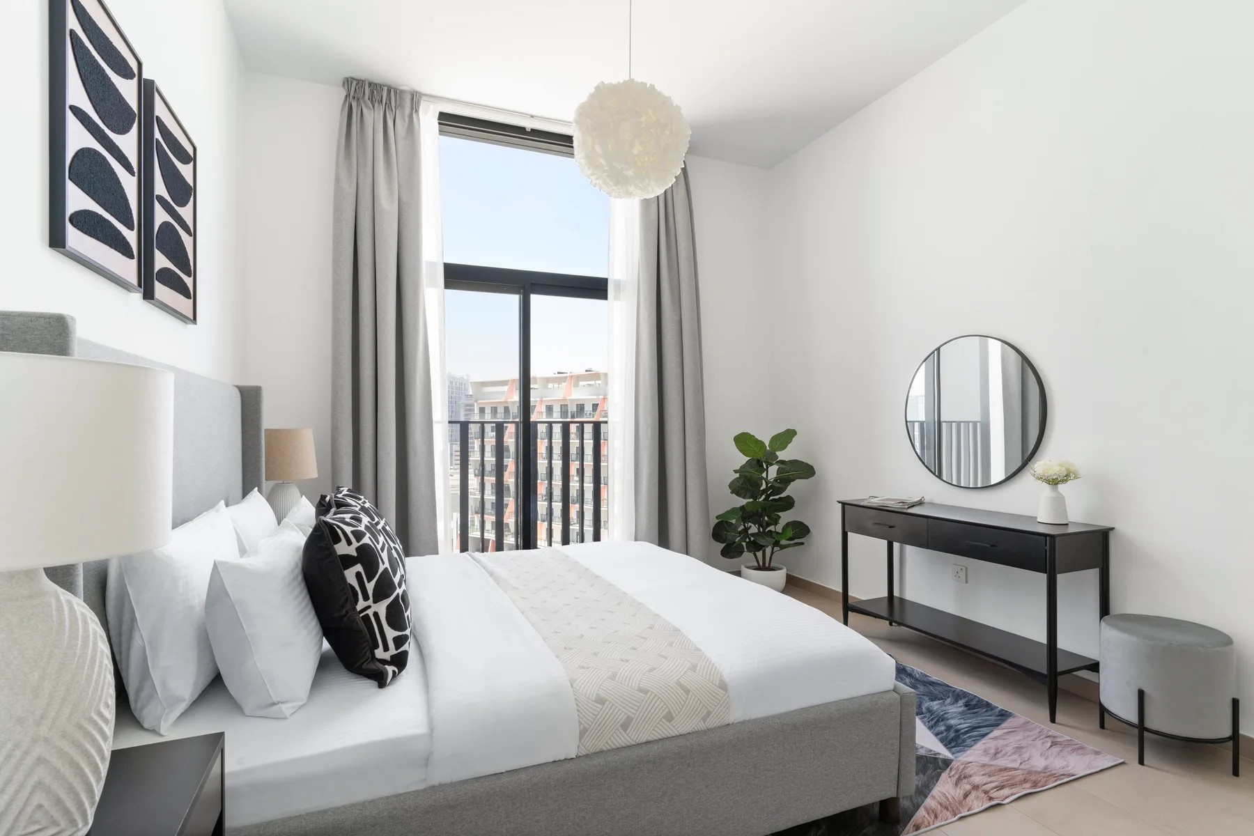A bright bedroom with a bed, tall window, and a small desk.