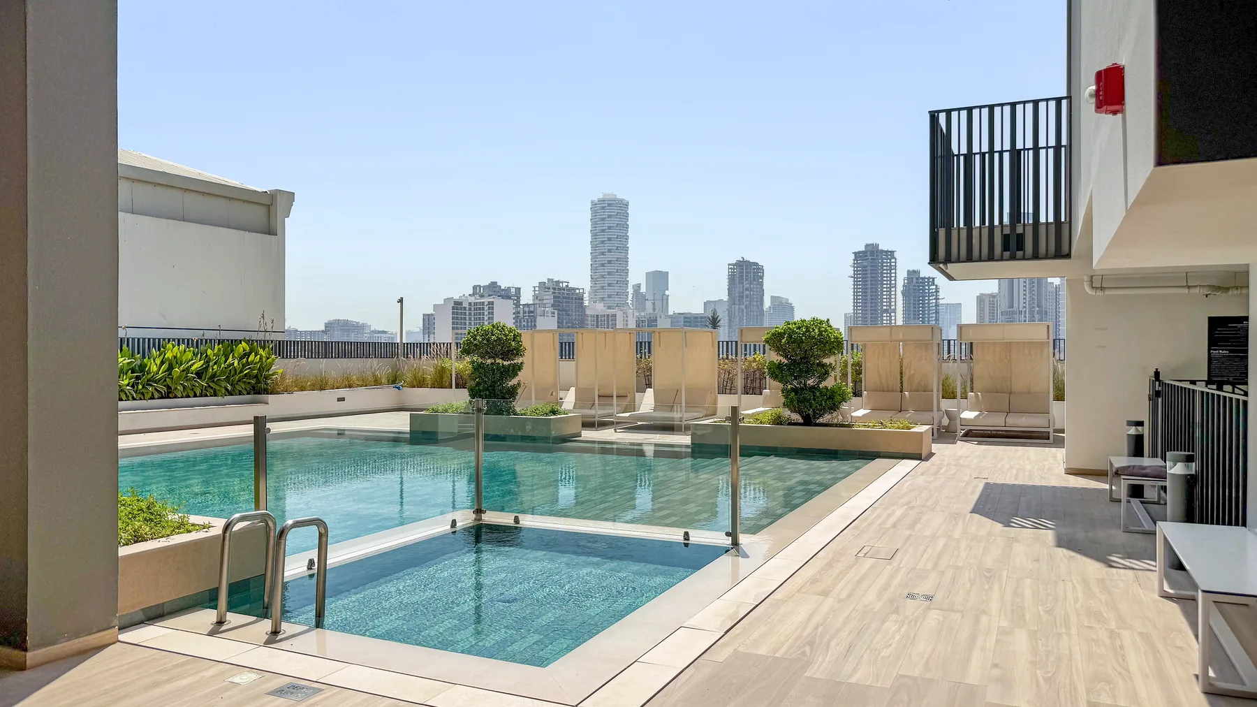 A rooftop pool area with lounge seating and city buildings in the distance.