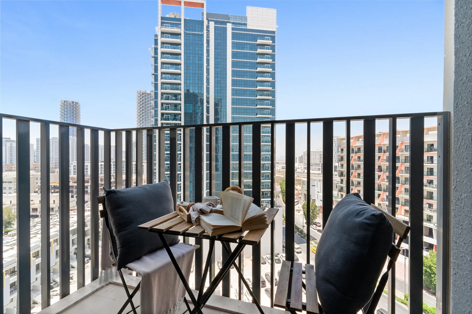 A balcony seating area with a small table overlooks nearby high-rise buildings.