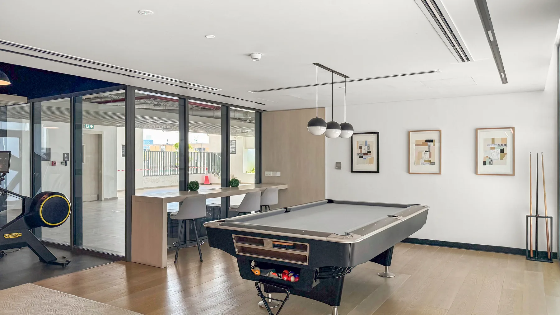 A modern recreation room features a pool table beside glass doors and a dining counter.