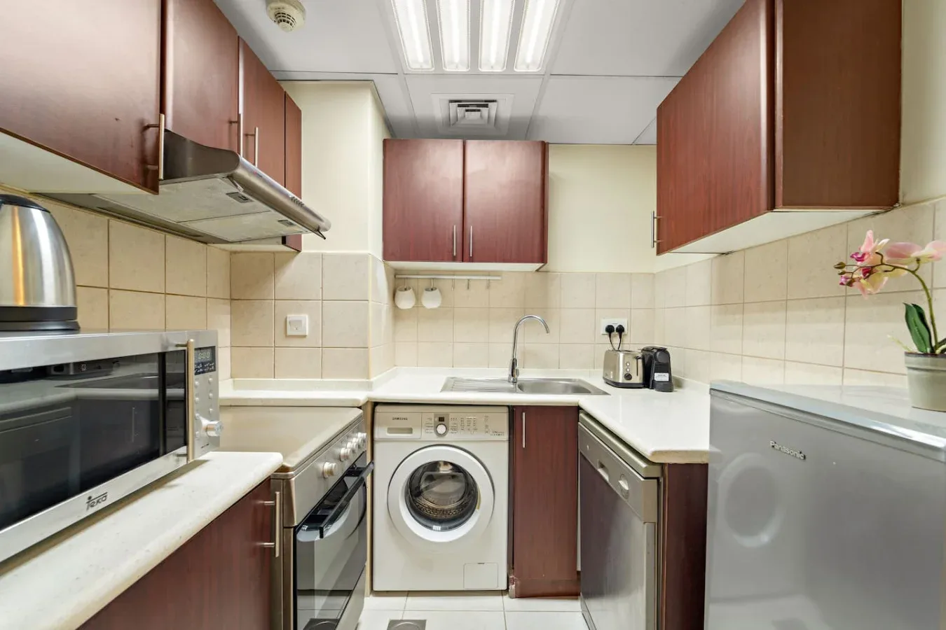 Una cocina compacta con gabinetes de madera, encimeras blancas y electrodomésticos integrados.