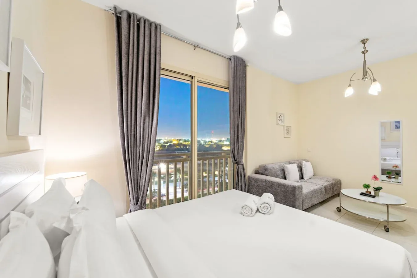 Un dormitorio luminoso con una cama grande junto a una ventana con vistas a las luces de la ciudad.