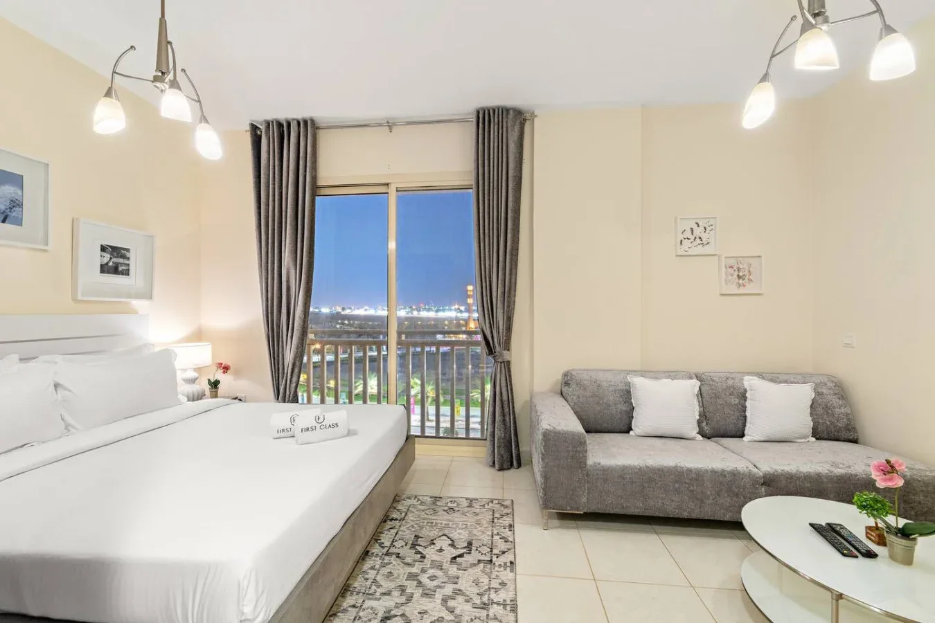 Un dormitorio con cama, asientos y una puerta de balcón con vistas a las luces de la ciudad.