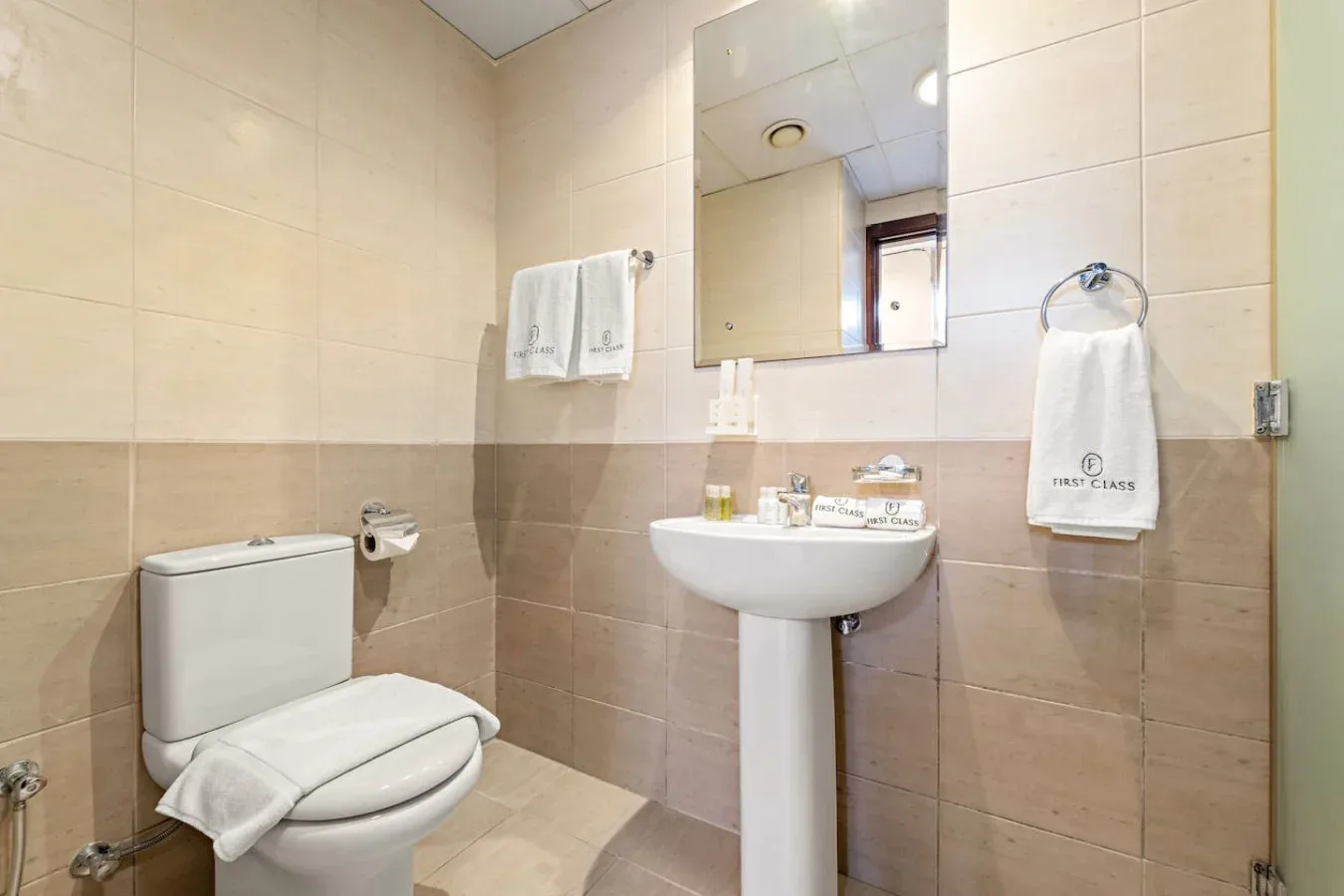 Un baño con azulejos, lavabo de pedestal, espejo e inodoro.