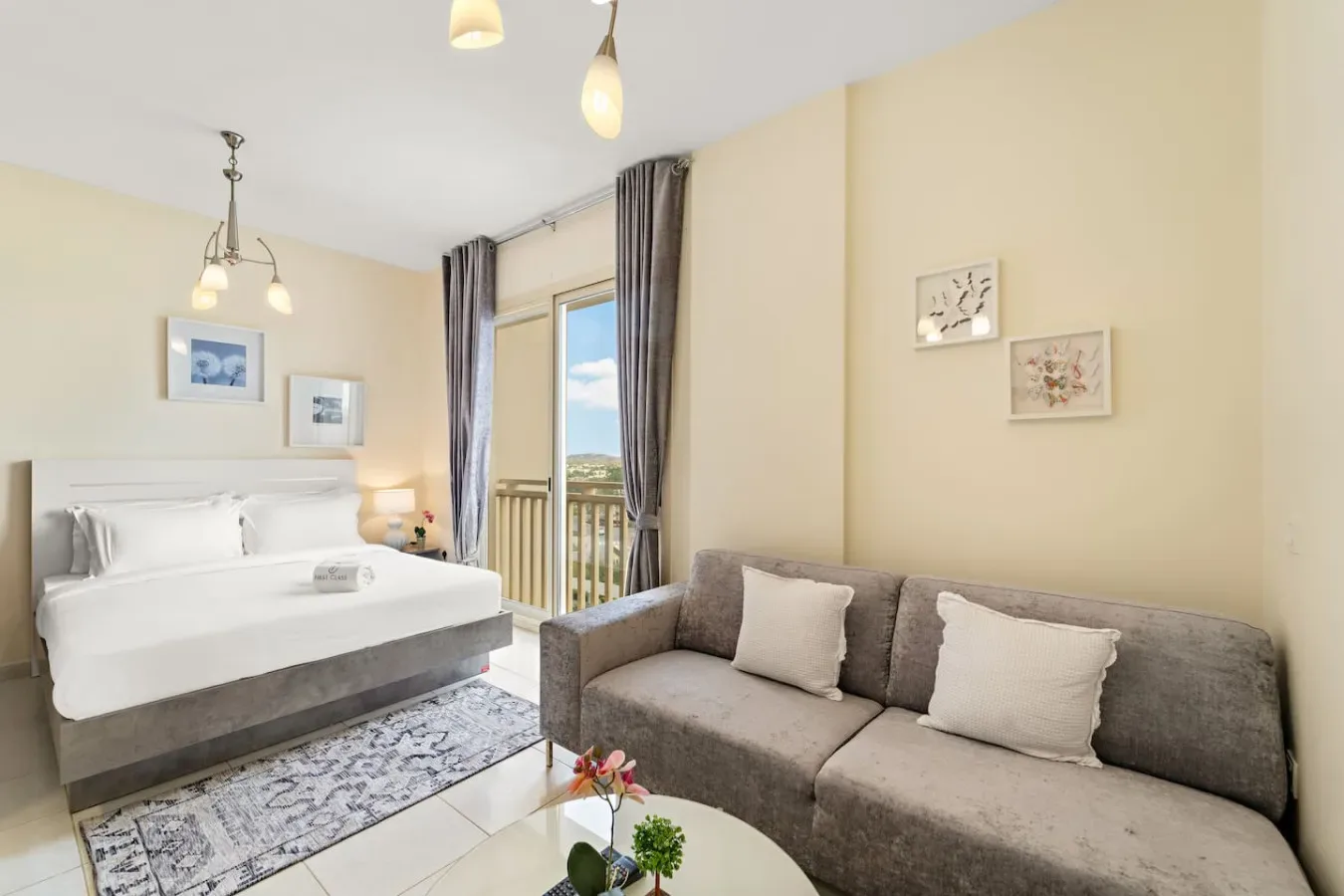 Un dormitorio con una cama junto a un sofá gris y una puerta de balcón con cortinas.