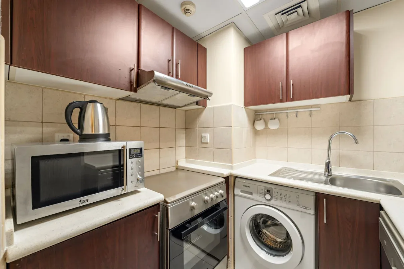 Una cocina compacta con microondas, estufa, lavadora y fregadero.