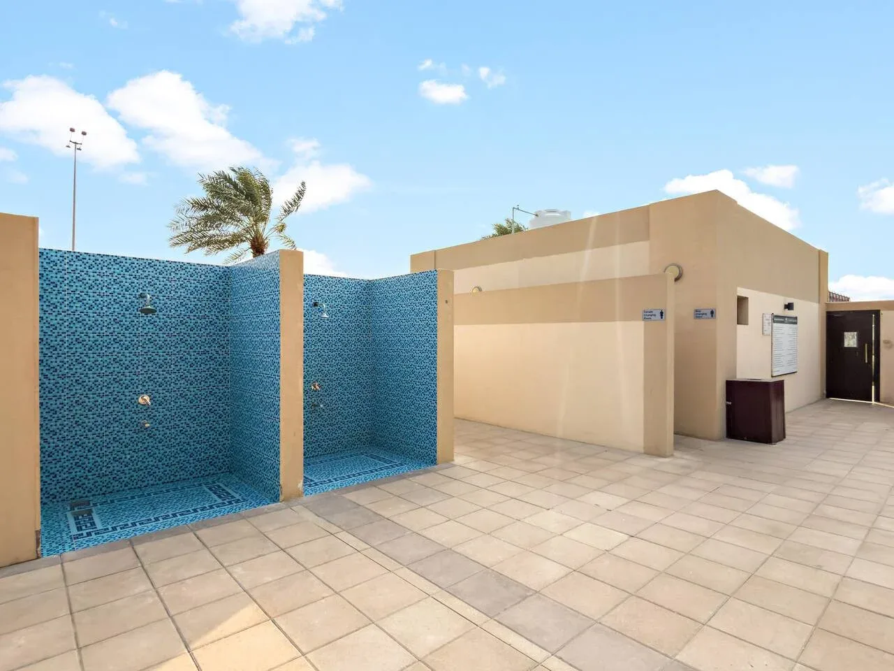 Zona de duchas al aire libre con paredes de azulejos azules junto a un camino pavimentado.