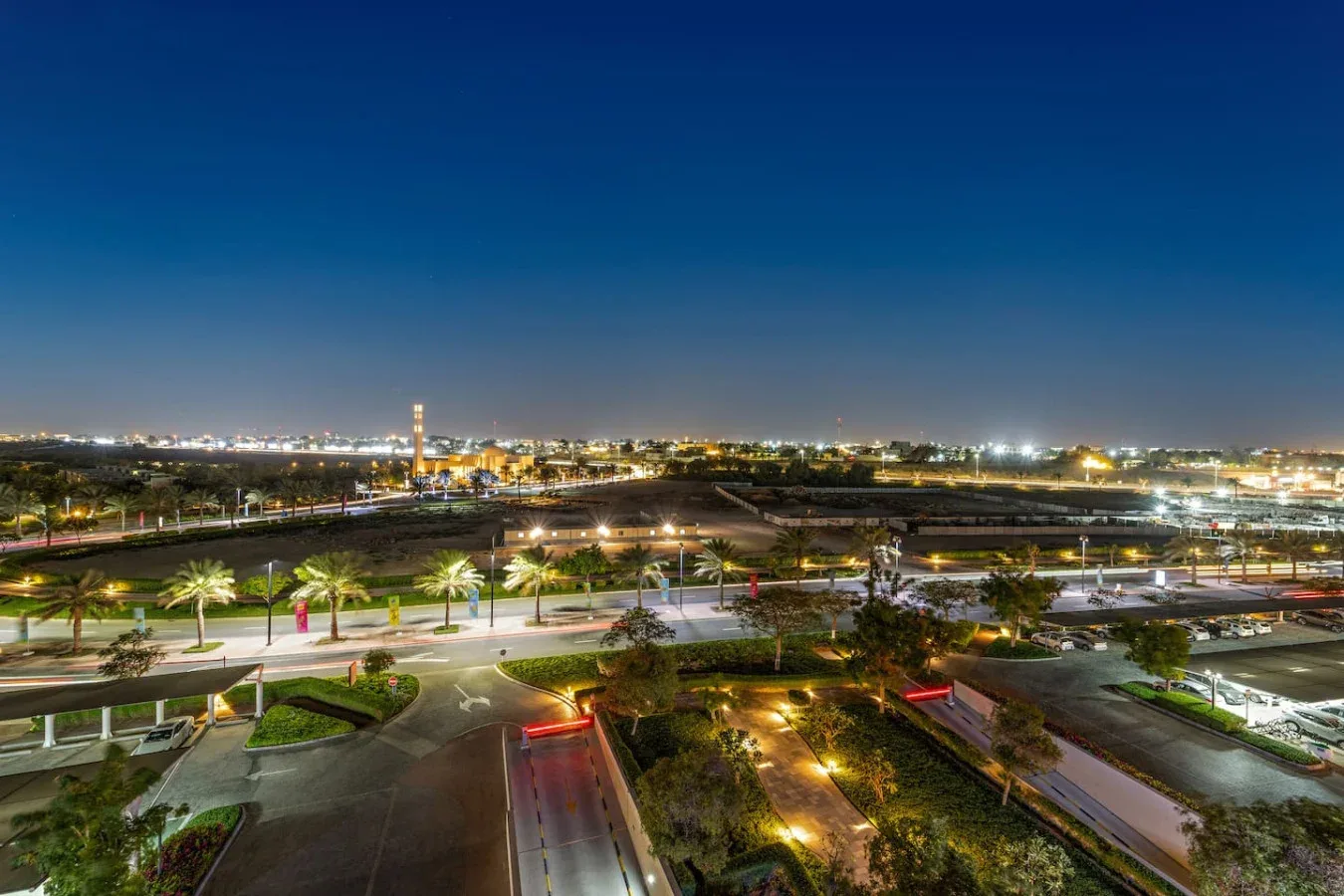 Paisaje urbano nocturno con carreteras iluminadas, zonas verdes y luces de la ciudad a lo lejos.