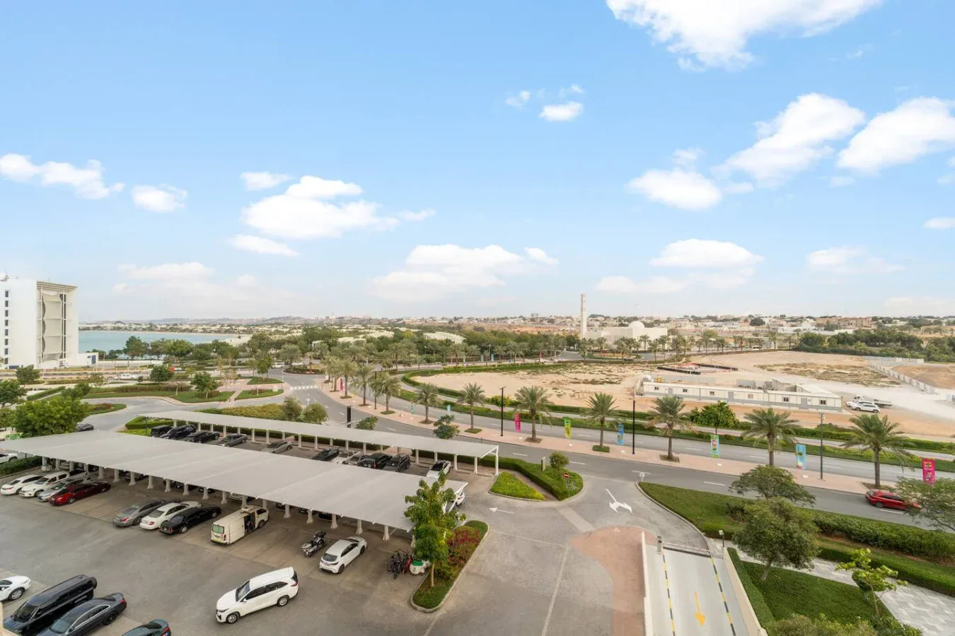 Una amplia vista urbana muestra calles, zonas ajardinadas y un estacionamiento bajo un cielo azul.