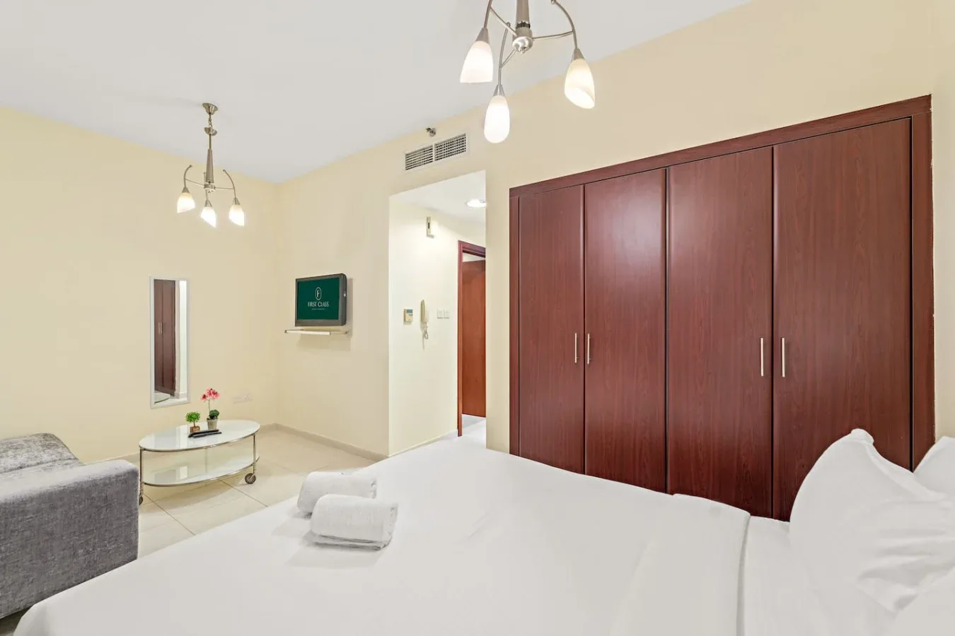 Un dormitorio con una cama blanca, un armario de madera oscura y una pequeña zona de estar.