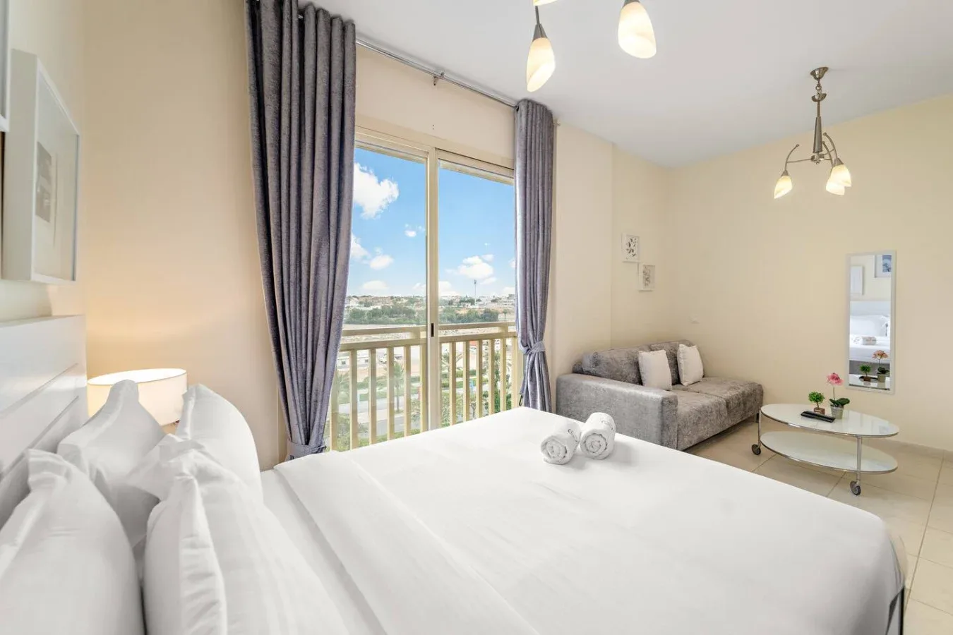 Un dormitorio luminoso con una cama tendida y una pequeña zona de estar junto a la ventana.