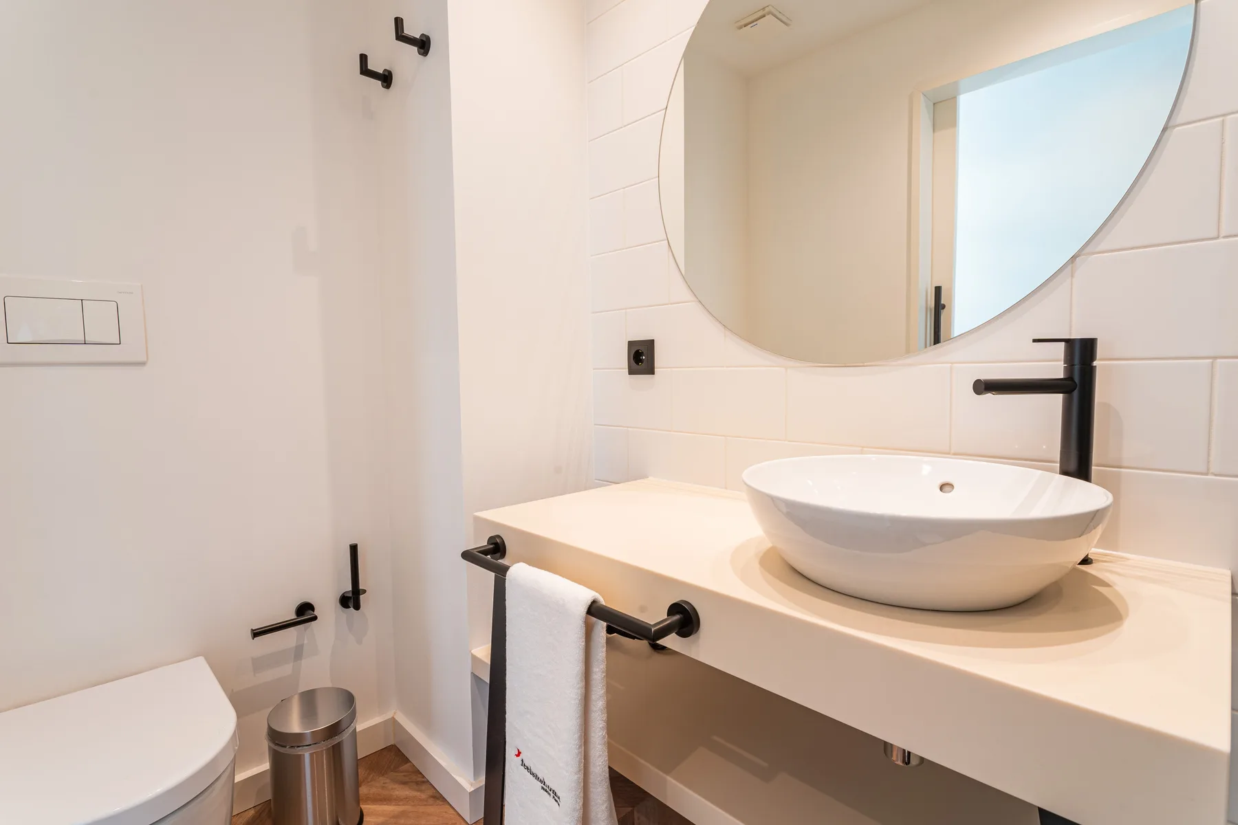 A bathroom with a white vessel sink beneath a large round mirror.